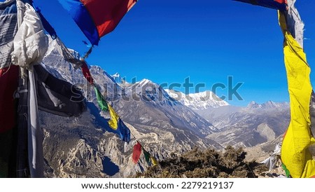 Waving flags with mantra 'Om mani padme hum' on them. Wind blows them over Himalayan peaks. Very weary flags. High Annapurna Chain peaks covered with snow. meditation and retreat