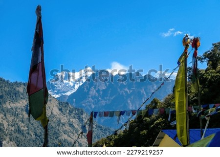 Colorful prayer flags waving above the Himalayan peaks along Annapurna Circuit Trek, Nepal. Meditation and peace of mind. High, snow caped mountains peaks catching the first beams of sunlight Royalty-Free Stock Photo #2279219257