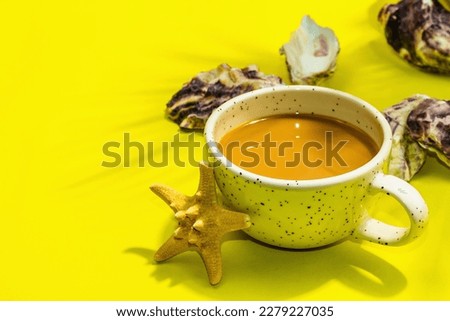 A cup of coffee in a marine style. Starfish, oysters, palm leaves. Hard light, dark shadow, bright yellow background, flat lay, copy space