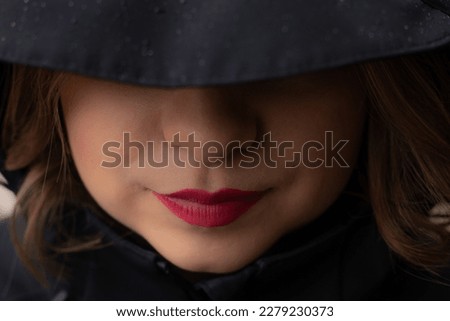 A woman with red lips in a black hoodie under the rain. Beautiful young woman under the hood. Young girl with beautiful red lips Royalty-Free Stock Photo #2279230373