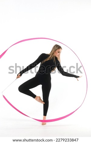 Girl gymnast in a black tight-fitting jumpsuit with a pink ribbon on a white background