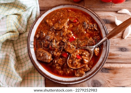 Pork goulash meat on plate, cutlery, garlic, onion, tablecloth in the background - typical Czech food Royalty-Free Stock Photo #2279252983