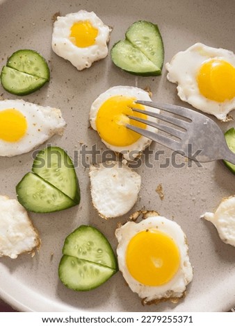 Artistic breakfast, beautiful food, a few small fried eggs on plate, slices of fresh cucumbers stacked in shape of heart. Bright colors, fresh food, healthy food, creative cooking. Top view. Food blog Royalty-Free Stock Photo #2279255371