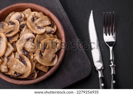 Fried or stewed champignon mushrooms in the form of slices with onions on a brown ceramic plate on a dark concrete background