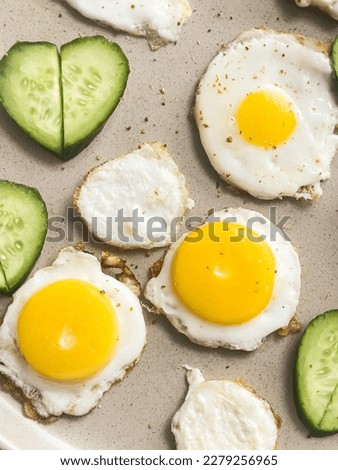 Artistic breakfast, delicious food, few small fried eggs on plate, slices of fresh cucumbers stacked in shape of heart. Bright colors, fresh, healthy meal, creative cooking. Top view. Food blog. Royalty-Free Stock Photo #2279256965