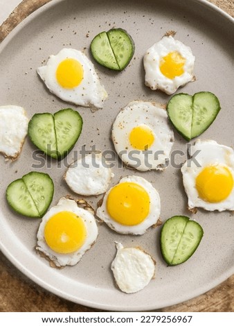 Artistic breakfast, delicious food, few small fried eggs on plate, slices of fresh cucumbers stacked in shape of heart. Bright colors, fresh, healthy meal, creative cooking. Top view. Food blog. Royalty-Free Stock Photo #2279256967
