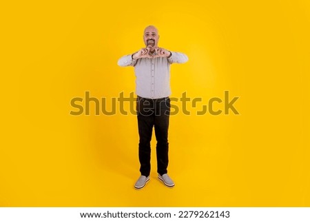 Making hearth symbol with hands. Caucasian middle aged  bald man, father figure making hearth symbol with hands over his chest. Standing studio yellow background. Full body shot. Copy space.