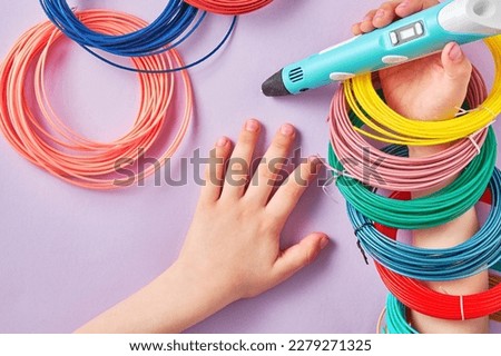 Kids hand with a new 3D pen and a bunch of plastic rings playing on the table. Hobby, toys and craft backgrounds. Banner with copy space for text