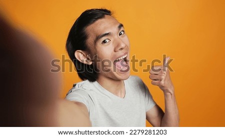 POV of positive adult taking photos on camera, acting funky and silly over orange backdrop. Young cool person posing for pictures in studio, smiling and being happy. Modern hipster.