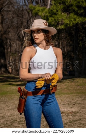 A beautiful brunette cowgirl poses outdoors on her farm before riding her horse Royalty-Free Stock Photo #2279285599
