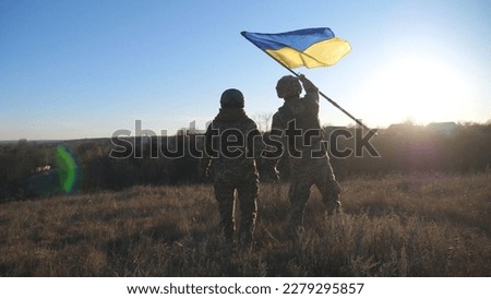 Dolly shot of young woman and man in military uniform waving flag of Ukraine against sunset. Female and male soldier of ukrainian army lifted blue-yellow banner holding hands of each other at field. Royalty-Free Stock Photo #2279295857
