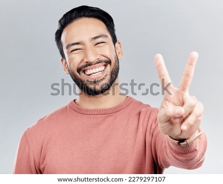 Portrait, peace sign and laughing Asian man in studio isolated on a gray background. Face, v emoji and happy, smiling or funny, young and confident male model with hand gesture or peaceful symbol.