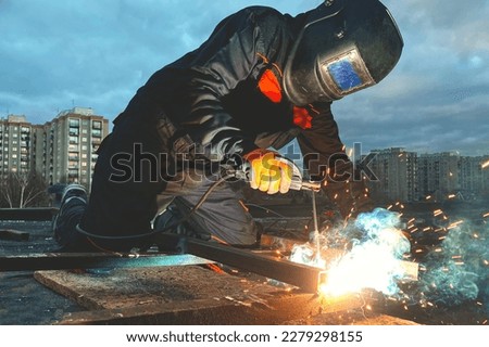 A welder in a suit and mask welds metal against the sky, welding work, a lot of sparks Royalty-Free Stock Photo #2279298155
