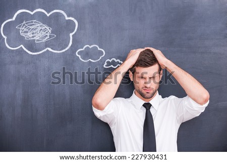 Mess in my head. Picture of confused handsome young man holding hands on head and keeping eyes closed while standing against cloud chalk drawing on blackboard