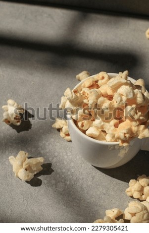 Popcorn in white cup under sunlight with shadow on grey background. Cinema snacks. Party time.