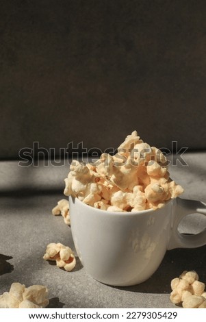 Popcorn in white cup under sunlight with shadow on grey background. Cinema snacks. Party time.
