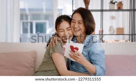 May Mother's day young adult grown up child cuddle hug give flower gift box red heart card to mature middle aged mum. Love kiss care mom asia people sitting at home sofa happy smile enjoy family time. Royalty-Free Stock Photo #2279311555