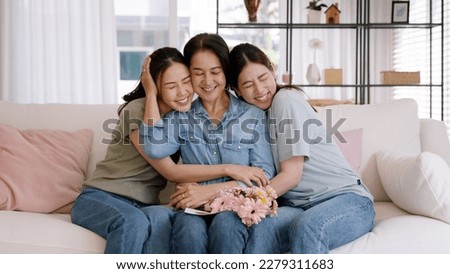 Happy time May Mother day cuddle hug care love face to face kiss cheek to mature mum. Asia middle aged old mom adult people smile enjoy receive gift flower from young child sitting at home sofa relax. Royalty-Free Stock Photo #2279311683