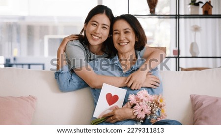 Happy time Mother day grown up child looking at camera cuddle hug give flower gift box red heart card to mature mum. Love kiss care mom asia middle age adult people smile enjoy sitting at home sofa. Royalty-Free Stock Photo #2279311813