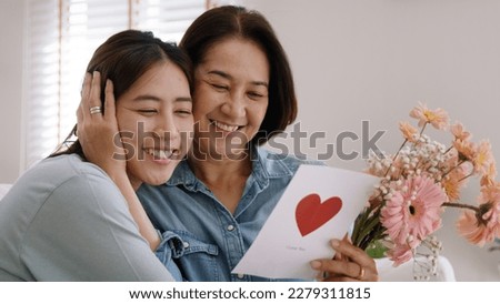 May Mother's day young adult grown up child cuddle hug give flower gift box red heart card to mature middle aged mum. Love kiss care mom asia people sitting at home sofa happy smile enjoy family time. Royalty-Free Stock Photo #2279311815