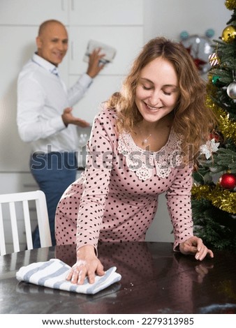 Young positive family couple preparing for New Year celebration, cleaning furniture