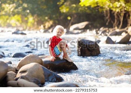Children hiking in Alps mountains crossing river. Kids play in water at mountain in Austria. Spring family vacation. Little boy on hike trail. Outdoor fun. Active recreation with children.