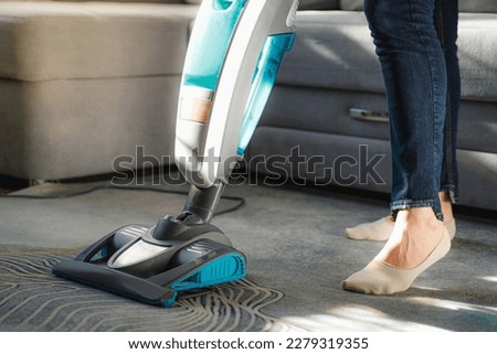 A young woman is vacuuming a carpet. House cleaning. Upright vacuum cleaner close-up. Faceless housewife in casual outfit with modern upright vacuum cleaner in minimalist light apartment Royalty-Free Stock Photo #2279319355