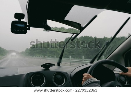 Person's hand holding the steering wheel and driving in the rain Royalty-Free Stock Photo #2279352063