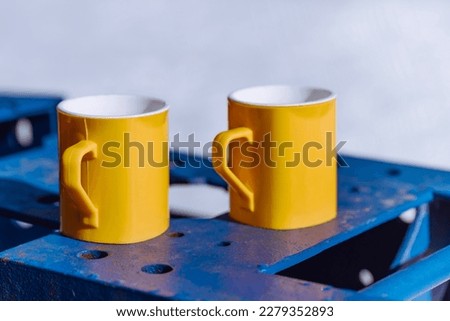 two yellow mugs with a hot drink on a metal structure on a winter day