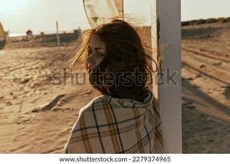 close-up portrait of a red-haired woman wrapped in a plaid in the rays of the setting sun, turned away from the camera
