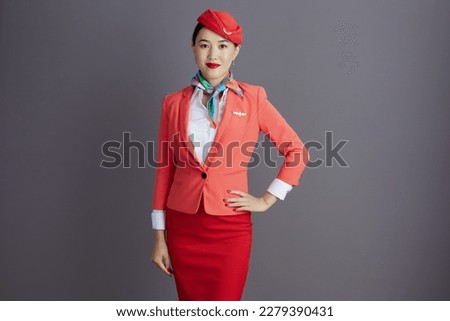modern asian female flight attendant in red skirt, jacket and hat uniform isolated on grey background. Royalty-Free Stock Photo #2279390431
