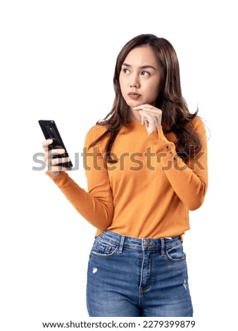 Photo features a happy Indonesian woman wearing an orange sweater and jeans while holding a smartphone, isolated on a white background.