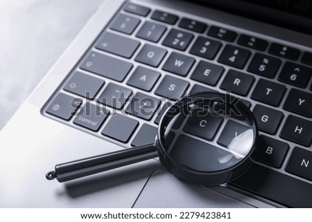 Magnifying glass and modern laptop on light grey table, closeup
