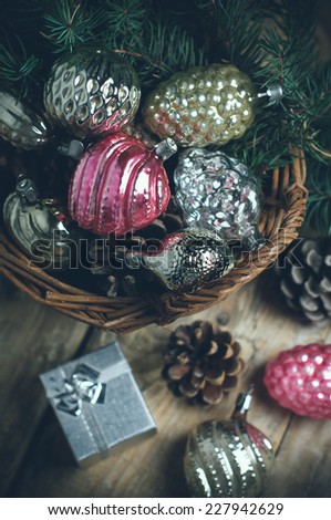 Vintage Christmas decorations and pine cones in a wicker basket, Christmas gift on a wooden table, faded colors