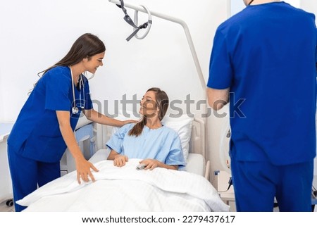 Hospitalized woman lying in bed while doctor checking on her. Doctor and nurse examining female patient in hospital room.