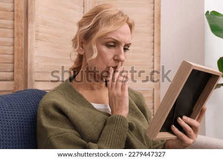 Upset middle aged woman with photo frame at home. Loneliness concept