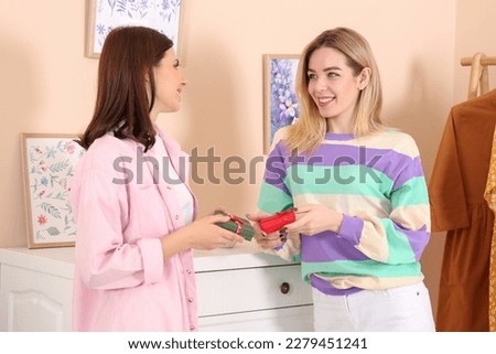 Smiling young women presenting gifts to each other indoors