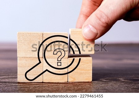 Faceless person putting set of wooden blocks on another for creating picture of question mark in magnifier
