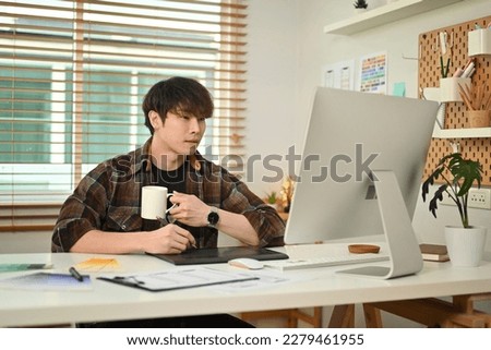 Young creative man looking at computer screen, planning application development at design studio