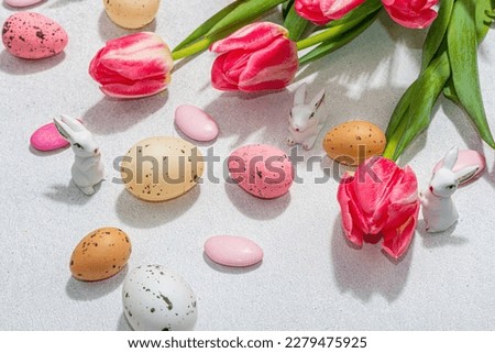 Pink tulips with Easter eggs and rabbits on light stone concrete background. Festive concept, greeting card, flat lay, hard light, dark shadow, close up