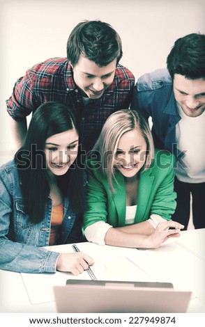 education concept - smiling students looking at laptop at school