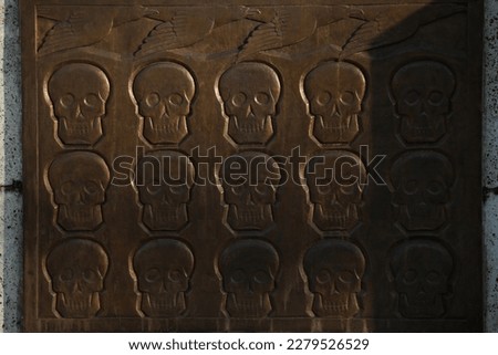 Brown metal plate with skulls and birds, fifteen skulls and five birds on the monument