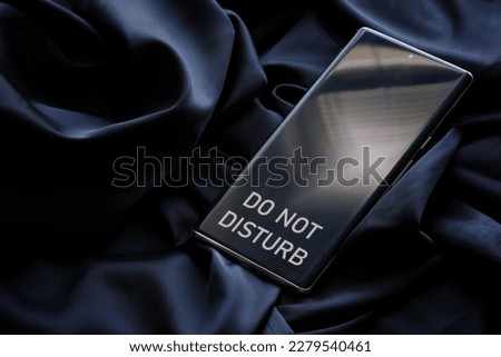 Modern smartphone with the inscription do not disturb on a dark background of cozy fabric. The concept of relaxation, solitude and introvert. Close-up Royalty-Free Stock Photo #2279540461