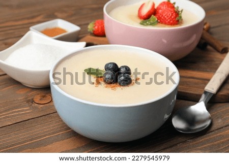 Bowls of tasty semolina porridge with strawberry and blueberry on wooden table Royalty-Free Stock Photo #2279545979