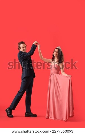 Beautiful couple dressed for prom dancing on red background