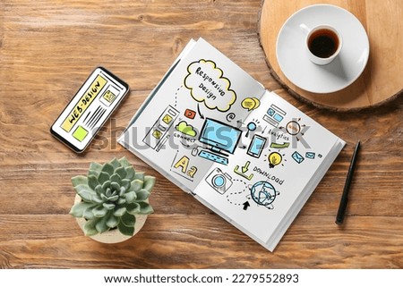 Notebook with sketches of web designer, mobile phone and cup of coffee on wooden background