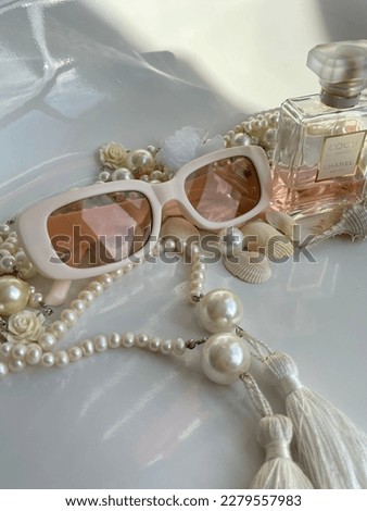 Aesthetic accessories in the foreground, in white and beige, glasses with perfume and pearls