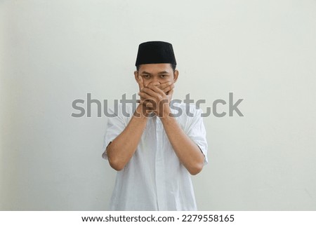 Serious young Asian Muslim man wearing Arabic costume standing with close on his mouth and doing rejection signs isolated on white background. People religious Islamic lifestyle concept