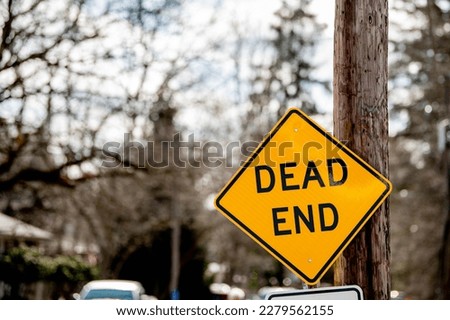 A dead end sign hangs by a utility pole on a roadway. 