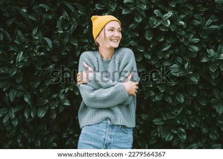 Photo of friendly smiling attractive woman on background of green hedge. Happy confident woman in front of green leaves wall. Thoughtful person outdoors at autumn season.